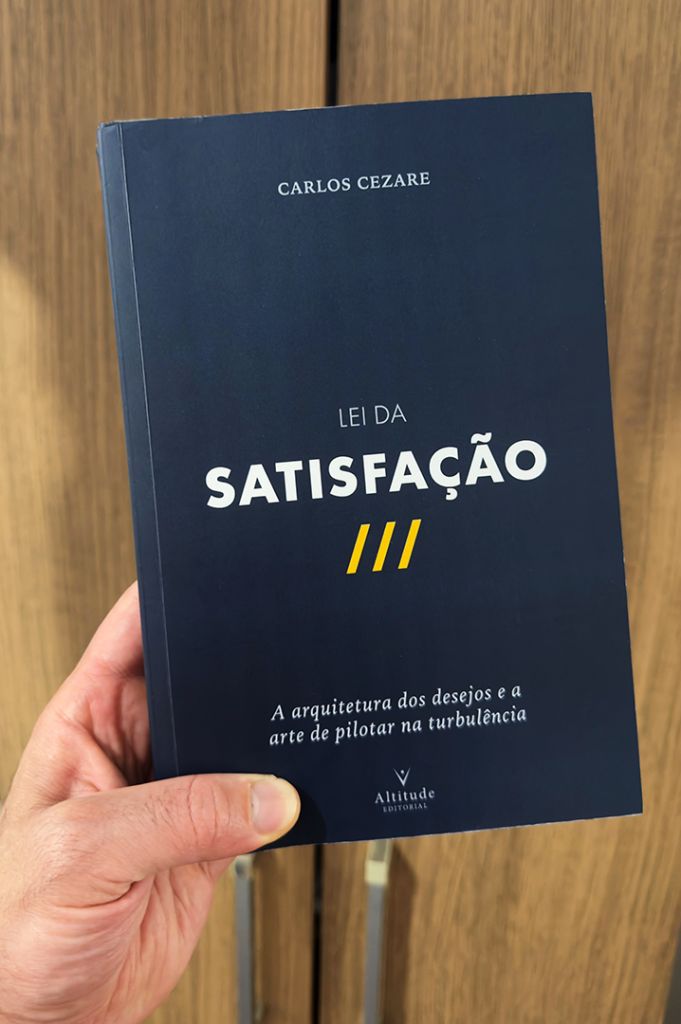 Carlos Cezare segurando a brochura azul-marinho de Lei da Satisfação